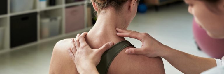 Fizjoterapeuta masuje kark i ramię pacjentki, która cierpi na ból kręgosłupa